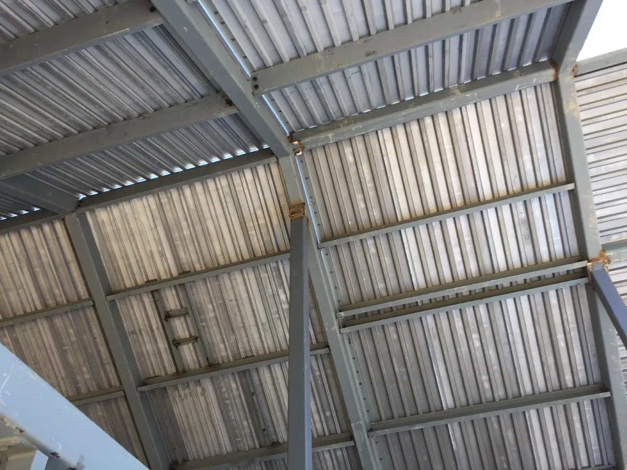 Steel roof framing with beams, purlins and metal decking, seen from below.